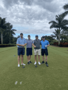 Four men standing on a golf course holding their clubs.