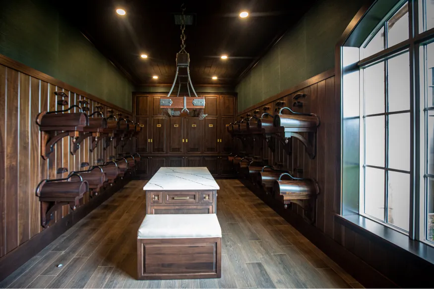 Room with wooden lockers and benches, wall-mounted storage units, a large window on the right, and a chandelier overhead.