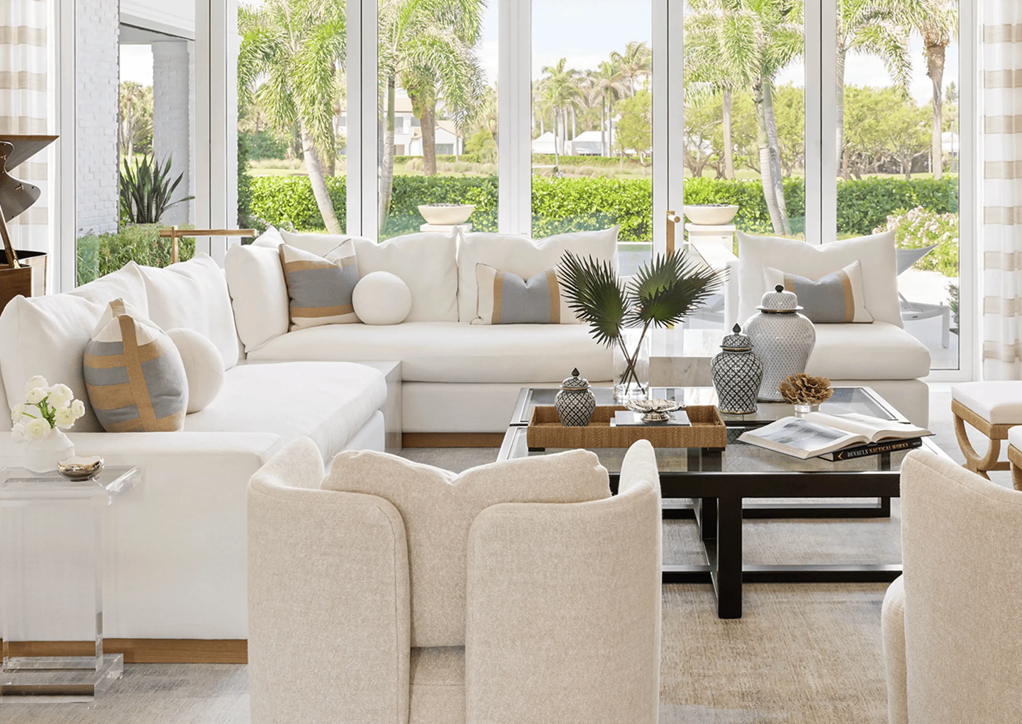 Living room with white furniture, including a sofa with pillows, chairs, a table with books, a flower vase