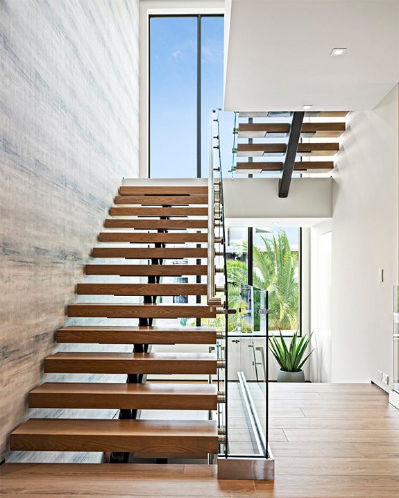 A wooden staircase with glass railing in the middle of it.